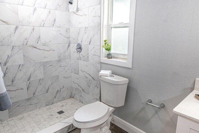 bathroom featuring toilet, vanity, and a tile shower