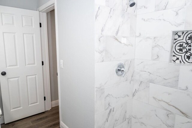 bathroom with a tile shower and wood-type flooring