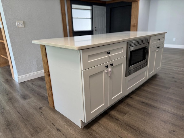 kitchen featuring baseboards, light countertops, stainless steel microwave, and dark wood finished floors