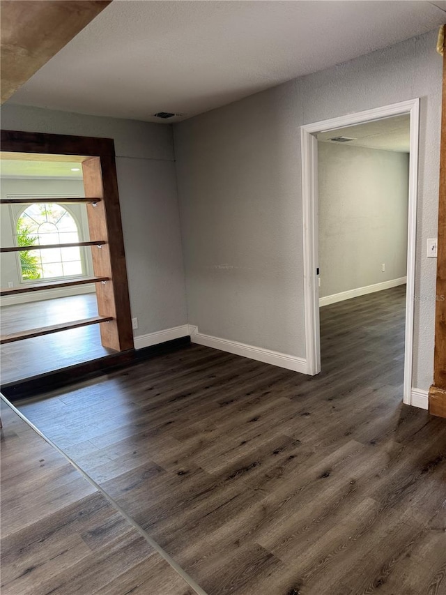 unfurnished room with baseboards, visible vents, and dark wood-type flooring