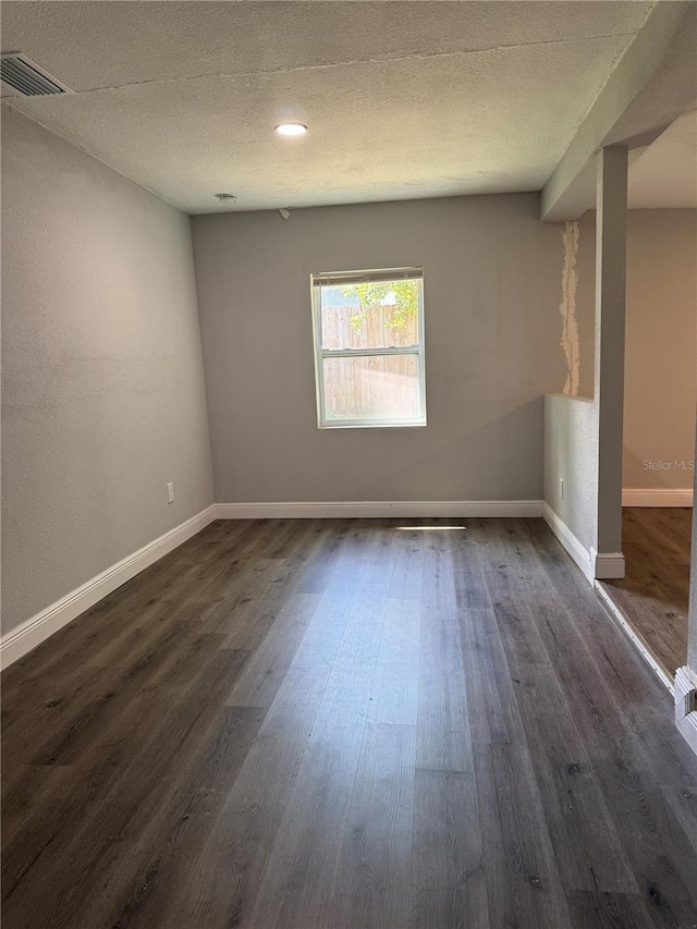 spare room featuring dark wood-style floors, visible vents, baseboards, and a textured ceiling