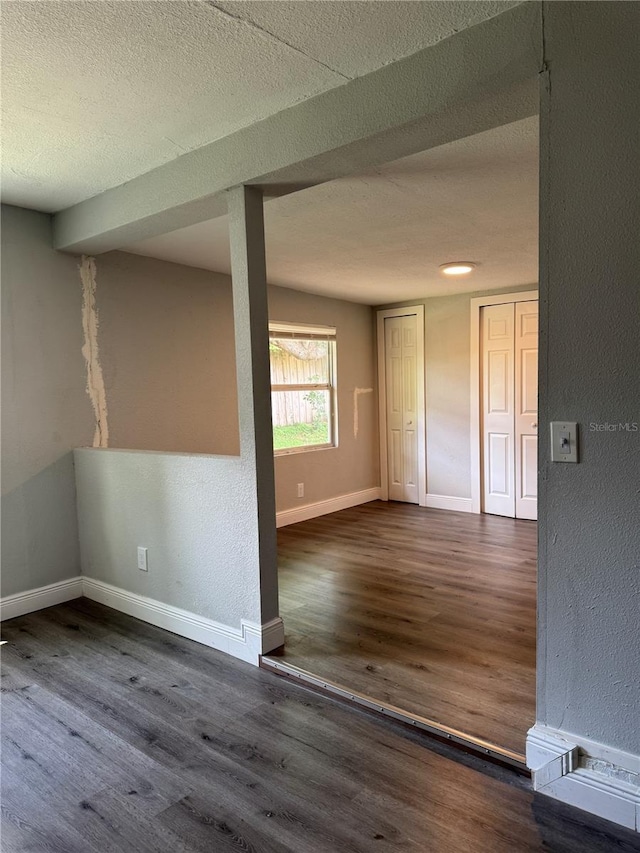 unfurnished room featuring a textured wall, a textured ceiling, baseboards, and wood finished floors