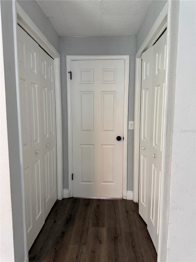 corridor with baseboards, dark wood-style flooring, and a textured ceiling