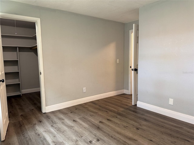 unfurnished bedroom featuring baseboards, a closet, wood finished floors, and a walk in closet