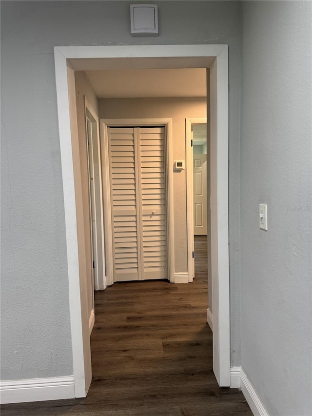 hall featuring baseboards, a textured wall, and dark wood-type flooring