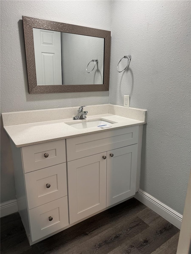 bathroom featuring vanity, a textured wall, baseboards, and wood finished floors