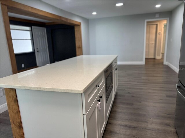 kitchen with a center island, dark wood-style floors, stainless steel microwave, baseboards, and recessed lighting