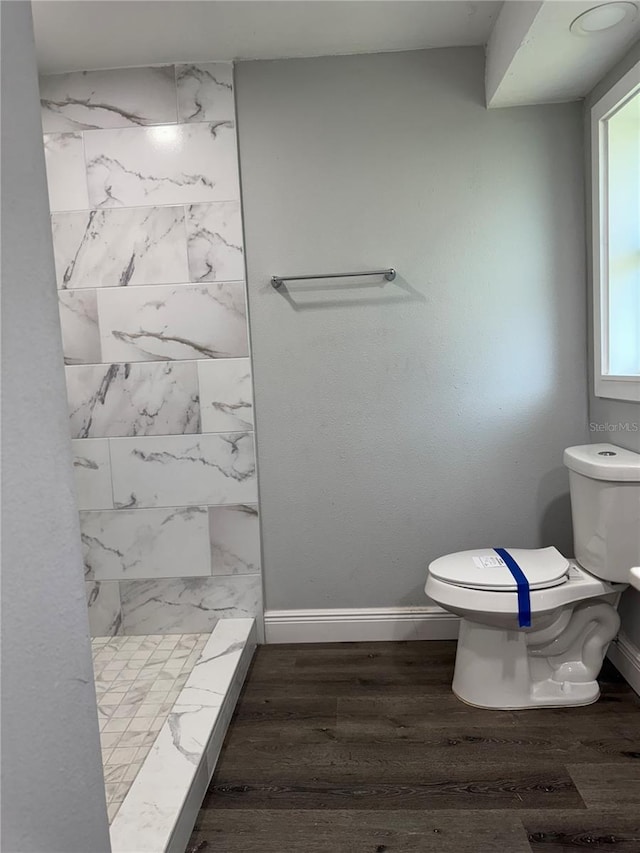 full bath featuring baseboards, wood finished floors, toilet, and tiled shower