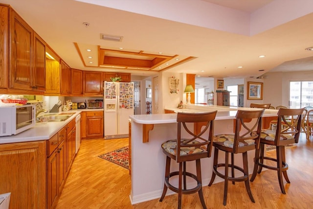 kitchen with a breakfast bar area, light hardwood / wood-style flooring, white appliances, sink, and a tray ceiling