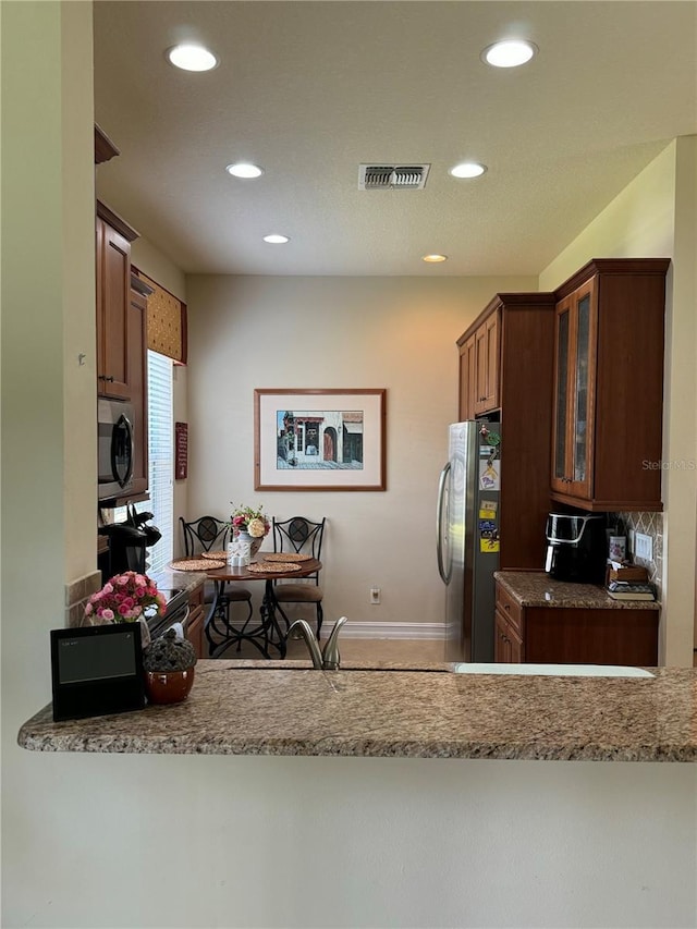 kitchen featuring visible vents, glass insert cabinets, a peninsula, light stone countertops, and stainless steel appliances