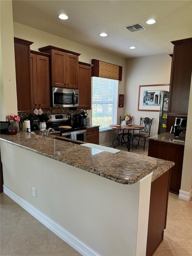 kitchen featuring light tile patterned flooring, stainless steel appliances, decorative backsplash, and kitchen peninsula