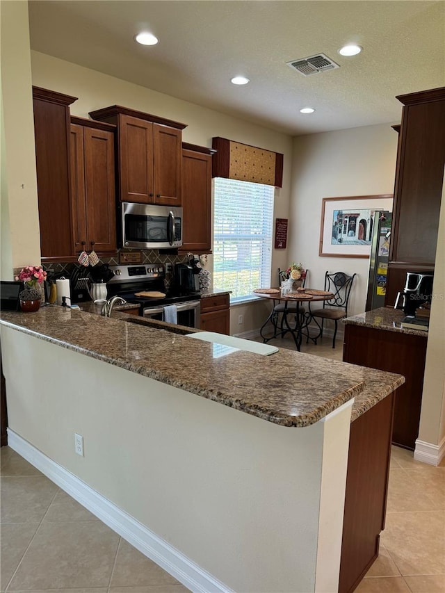 kitchen featuring a peninsula, visible vents, appliances with stainless steel finishes, backsplash, and dark stone countertops