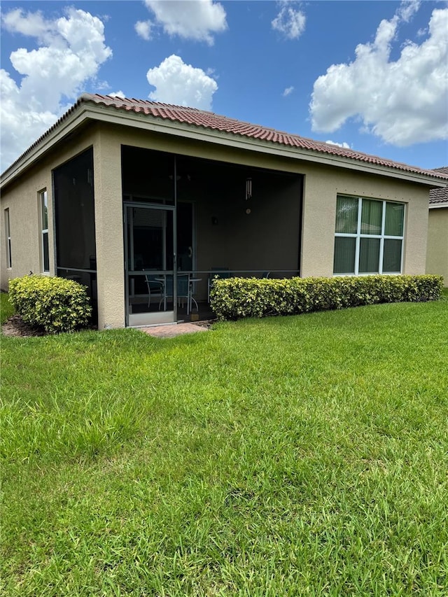 rear view of property with a sunroom, a lawn, and stucco siding