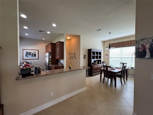 15953 Cobble Mill Dr, Wimauma, FL 33598 - kitchen featuring freestanding refrigerator, light tile patterned floors, glass insert cabinets, a textured ceiling, and light stone counters