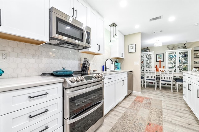 kitchen with appliances with stainless steel finishes, decorative light fixtures, white cabinetry, tasteful backsplash, and light stone counters