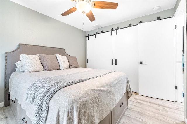 bedroom featuring ceiling fan, a barn door, and light hardwood / wood-style flooring