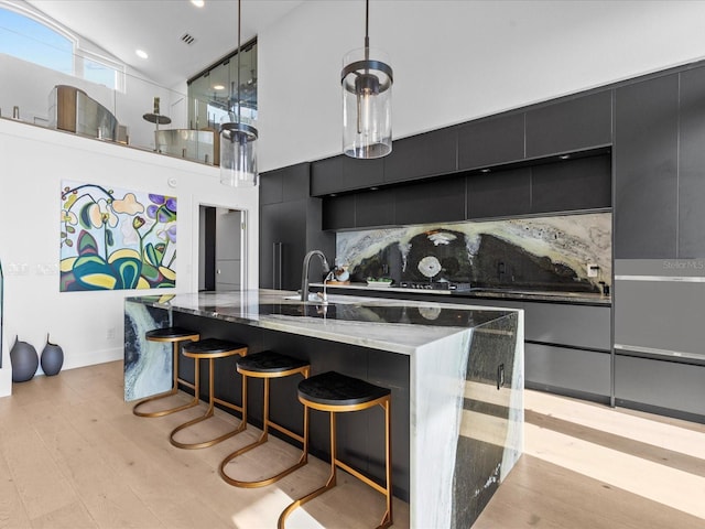 kitchen featuring high vaulted ceiling, a spacious island, decorative backsplash, decorative light fixtures, and light wood-type flooring