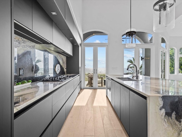 kitchen featuring pendant lighting, sink, stainless steel gas cooktop, light wood-type flooring, and french doors