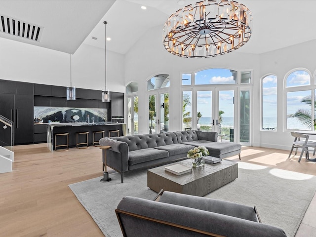 living room featuring a notable chandelier, high vaulted ceiling, french doors, and light wood-type flooring