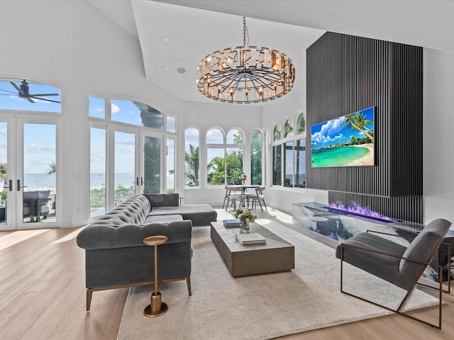 living room featuring a high ceiling, a notable chandelier, a water view, light wood-type flooring, and french doors