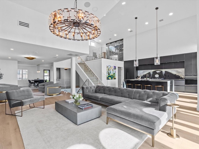 living room featuring an inviting chandelier, sink, a towering ceiling, and light wood-type flooring