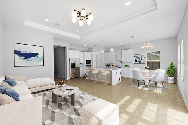 living room featuring crown molding, a chandelier, light wood-type flooring, and a raised ceiling