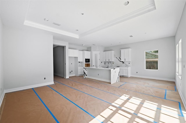 unfurnished living room with a raised ceiling and ornamental molding