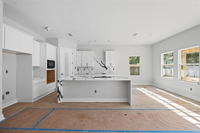 kitchen with an island with sink, black microwave, white cabinets, and tasteful backsplash