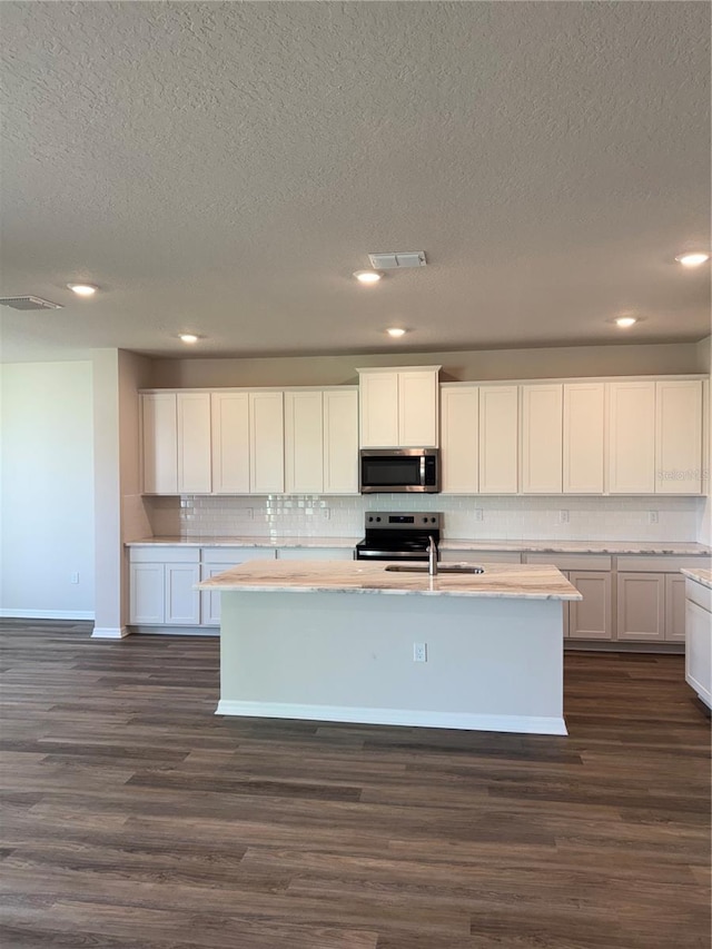 kitchen featuring stainless steel appliances, tasteful backsplash, a kitchen island with sink, light countertops, and a textured ceiling