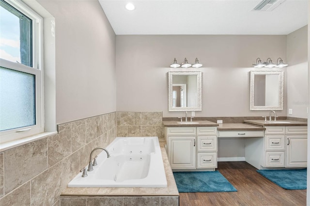 bathroom featuring hardwood / wood-style flooring, plenty of natural light, vanity, and tiled tub