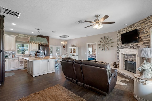 living room featuring dark wood-type flooring, ceiling fan, a fireplace, and a textured ceiling