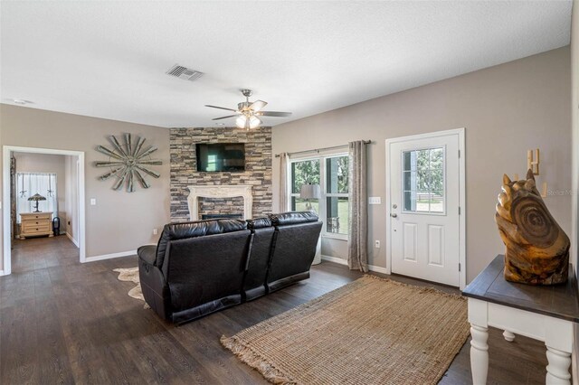 living room featuring dark wood-type flooring, ceiling fan, a stone fireplace, and a textured ceiling