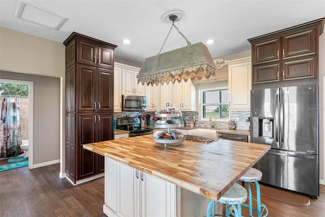 kitchen featuring a center island, stainless steel appliances, decorative backsplash, dark wood-type flooring, and butcher block countertops