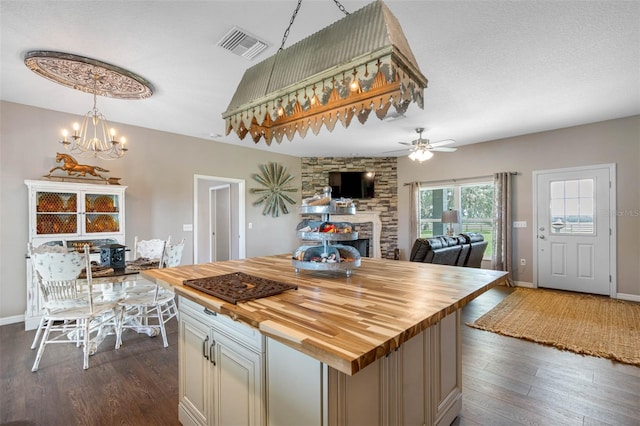 kitchen featuring a kitchen island, ceiling fan with notable chandelier, a fireplace, butcher block counters, and dark wood-type flooring