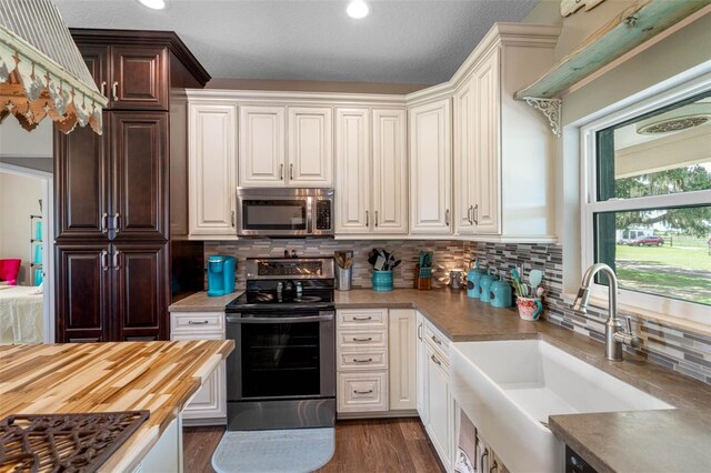 kitchen with sink, dark wood-type flooring, wooden counters, appliances with stainless steel finishes, and backsplash