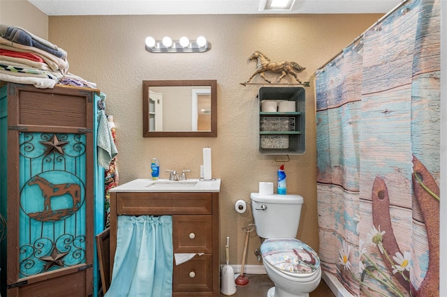 bathroom with a textured wall, vanity, toilet, and baseboards