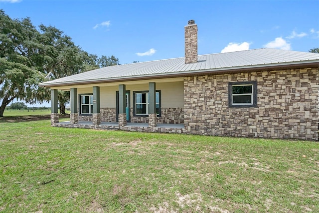 back of house featuring stone siding, a yard, a chimney, and metal roof