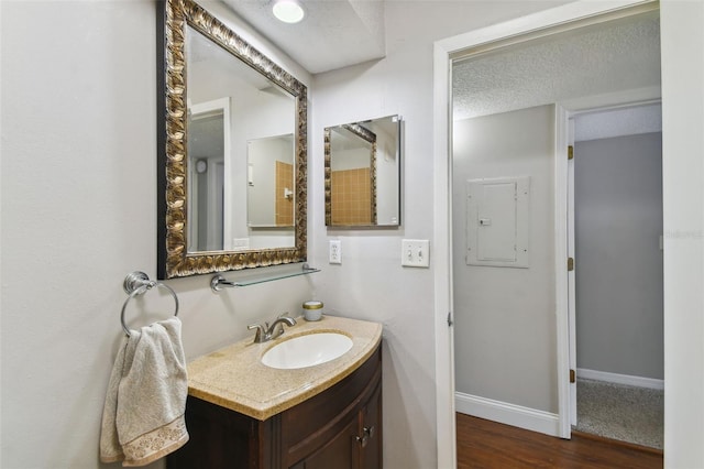 bathroom with a textured ceiling, vanity, wood-type flooring, and electric panel