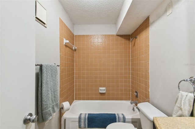 full bathroom with a textured ceiling, toilet, vanity, and tiled shower / bath