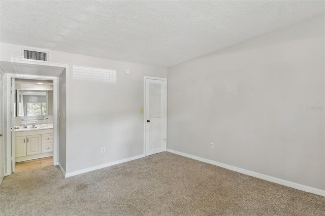 unfurnished bedroom featuring ensuite bath, sink, light carpet, and a textured ceiling