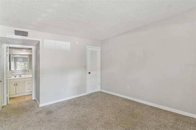 unfurnished bedroom featuring light carpet, baseboards, visible vents, connected bathroom, and a textured ceiling