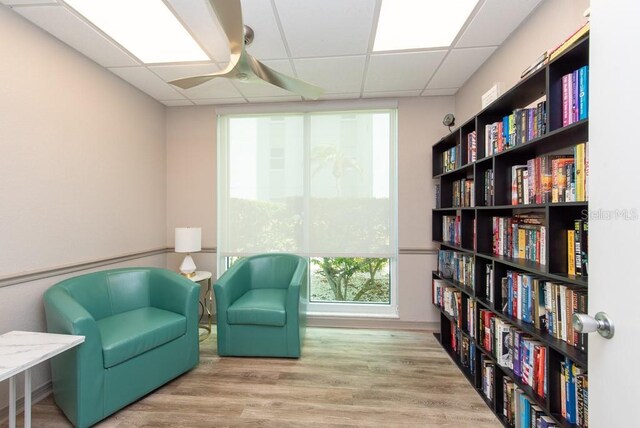 sitting room with a drop ceiling, ceiling fan, and light wood-type flooring