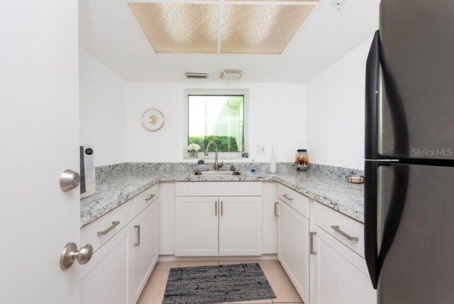 kitchen featuring light stone countertops, sink, white cabinetry, stainless steel refrigerator, and light tile patterned flooring