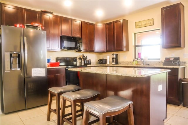 kitchen with a breakfast bar, black appliances, light tile patterned floors, and a center island