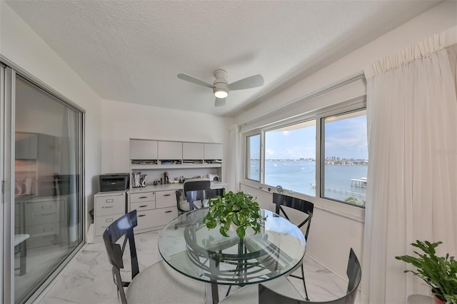 dining room with a water view, ceiling fan, and a textured ceiling