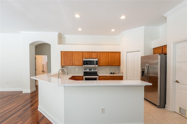 kitchen featuring crown molding, tasteful backsplash, kitchen peninsula, stainless steel appliances, and light hardwood / wood-style floors