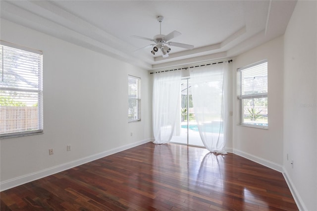 spare room with a raised ceiling, ceiling fan, and dark hardwood / wood-style flooring