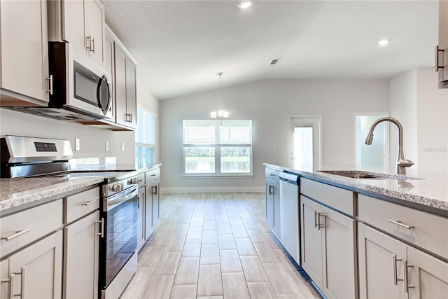 kitchen with an inviting chandelier, sink, vaulted ceiling, appliances with stainless steel finishes, and light stone counters