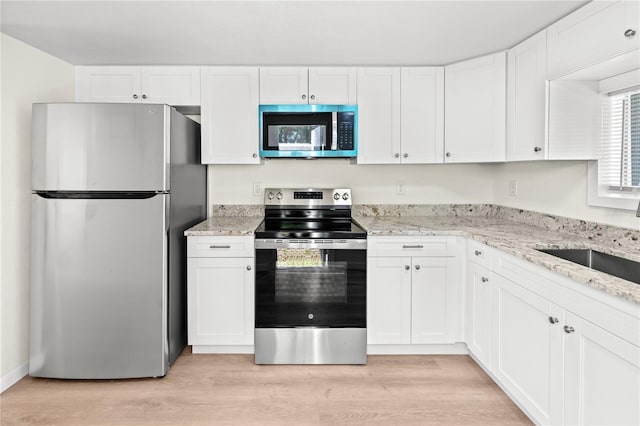 kitchen with sink, light hardwood / wood-style flooring, appliances with stainless steel finishes, light stone countertops, and white cabinets