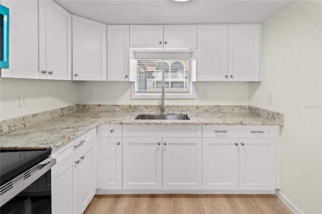 kitchen with light stone countertops, sink, white cabinets, and light hardwood / wood-style flooring